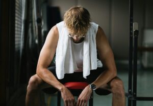 photo of man with a towel on his neck, sitting on a gym bench and looking down