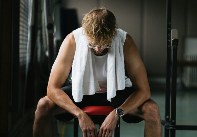 photo of man with a towel on his neck, sitting on a gym bench and looking down