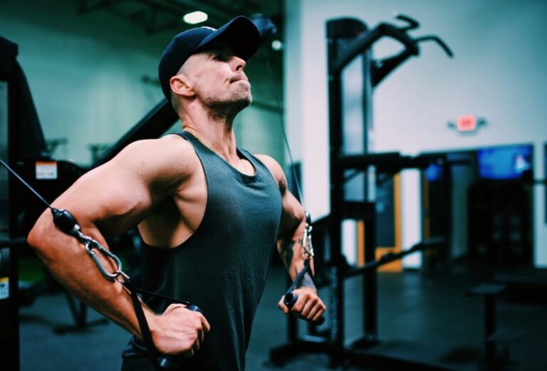 a muscular man wearing a tank top and cap, performing cable chest fly in a gym